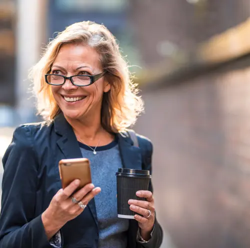 Smilende kvinne med telefon og kaffe i hånden, nyter en hyggelig stund